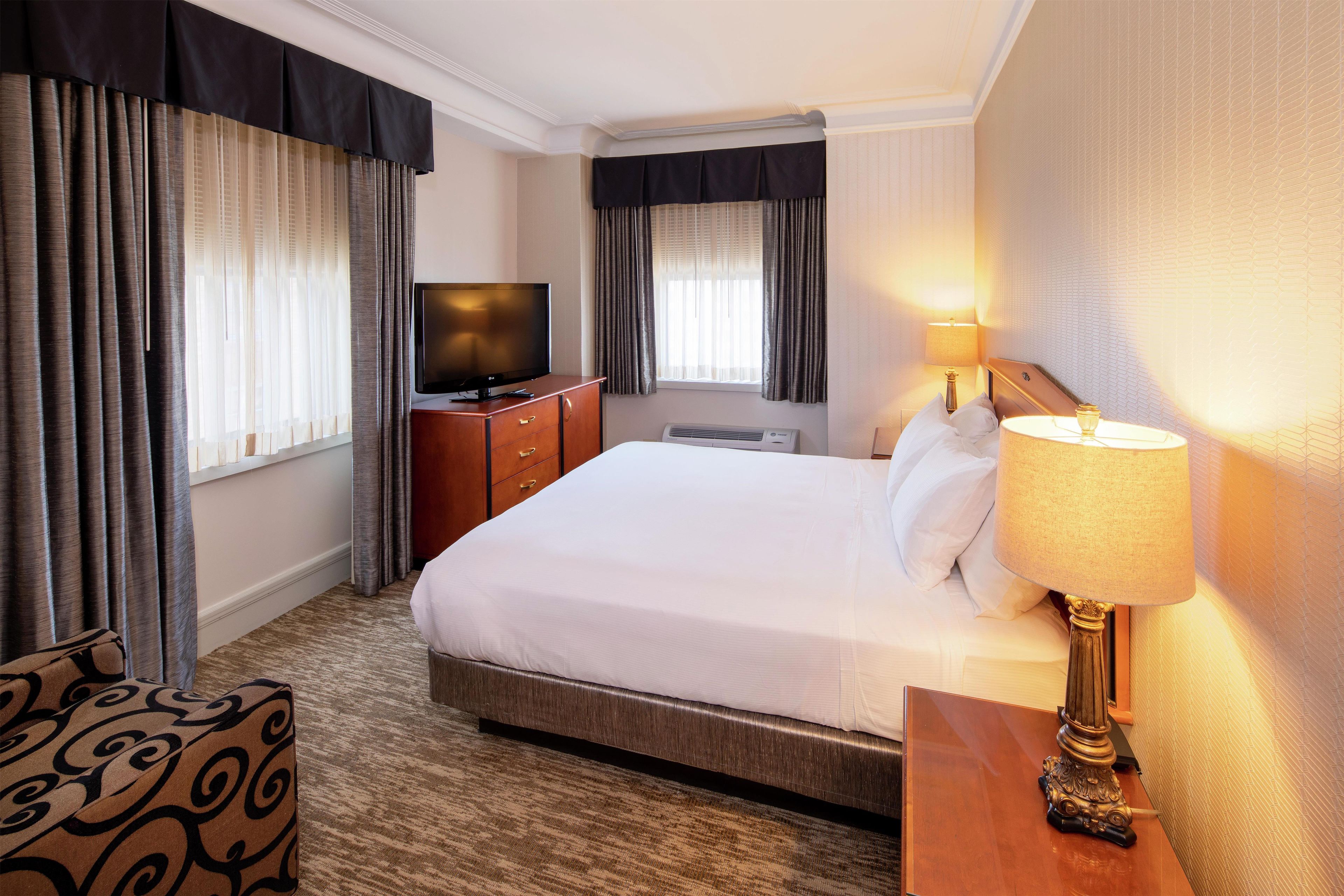 A hotel room with a bed, a television, a desk with a lamp, and a chair.