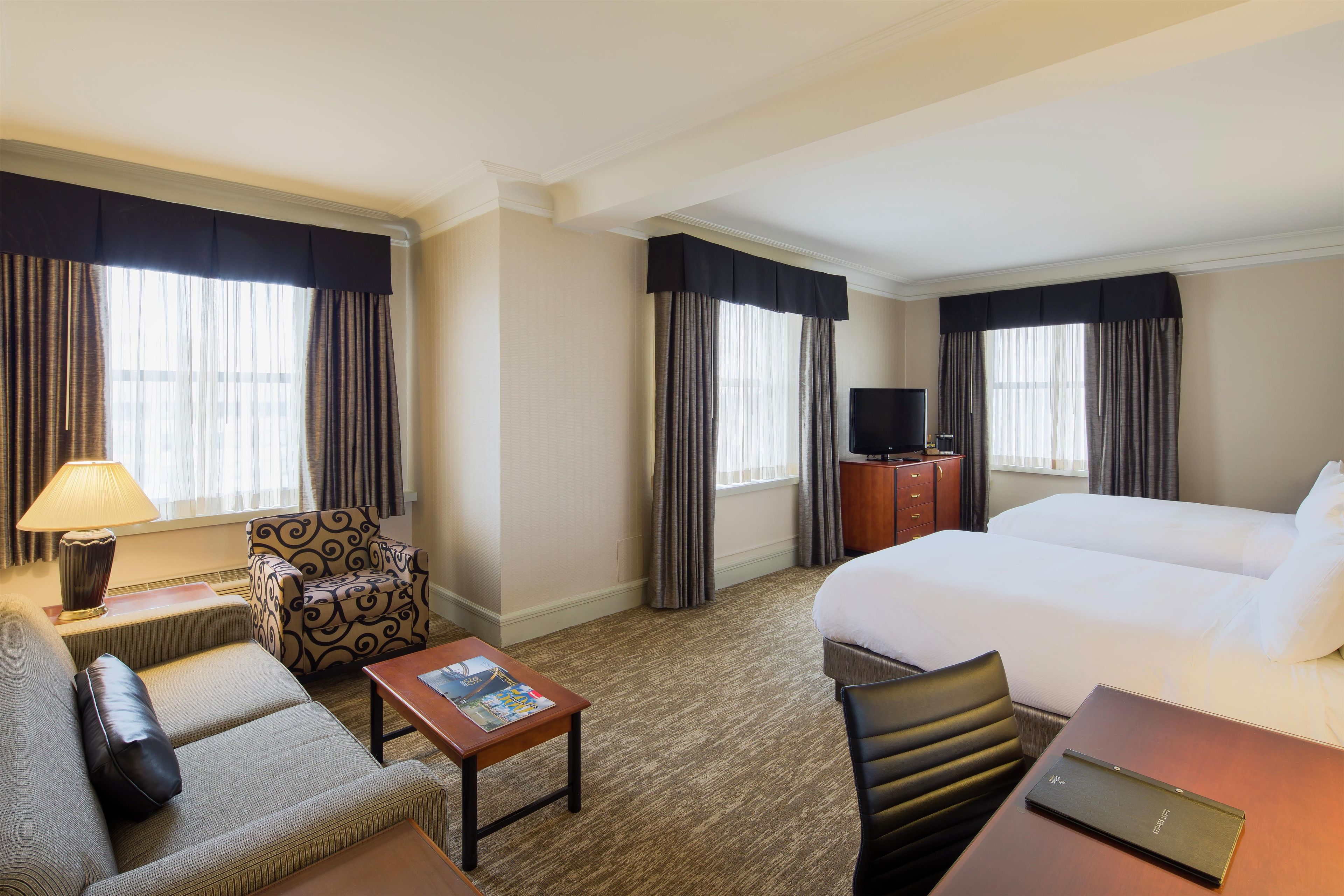A hotel room with a bed, a desk, a chair, a TV, and a lamp.