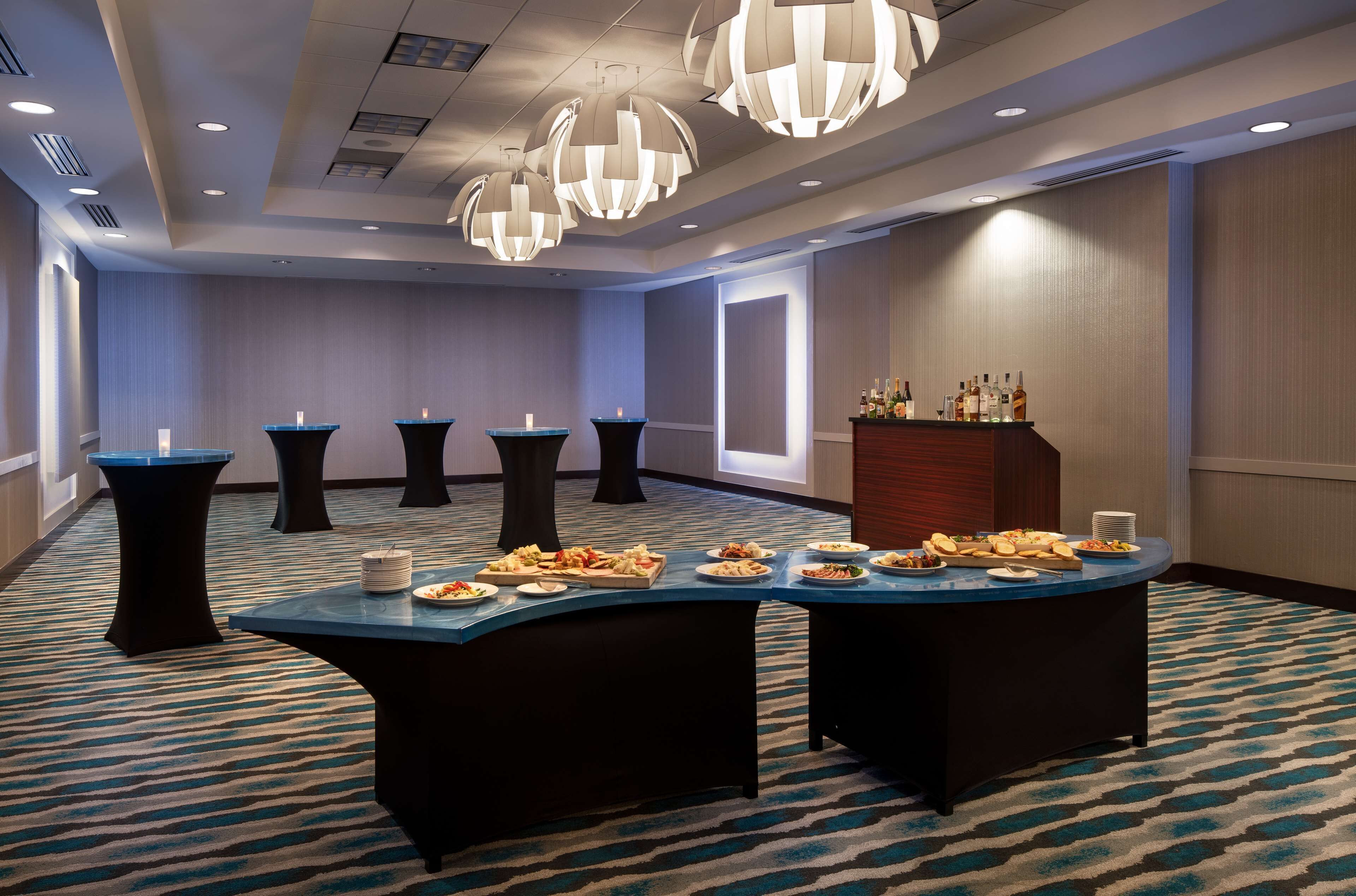 A conference room with a long table set for a meal, surrounded by black tables, and a bar area with bottles.