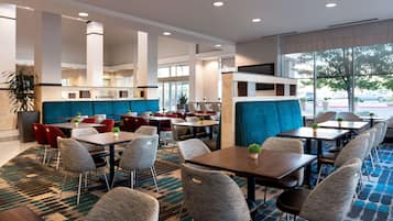 A modern restaurant with high tables and chairs, a blue accent wall, and large windows offering a view of the parking area.