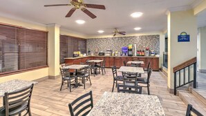 A restaurant with granite tables and chairs, a kitchen area, and a staircase leading to an upper level.