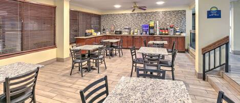 A restaurant with granite tables and chairs, a kitchen area, and a staircase leading to an upper level.