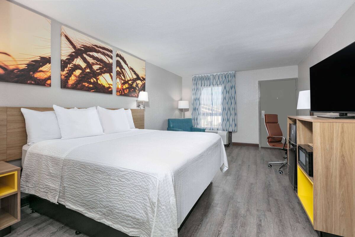 A hotel room with a large bed, a desk with a computer, a TV, and artwork on the wall.