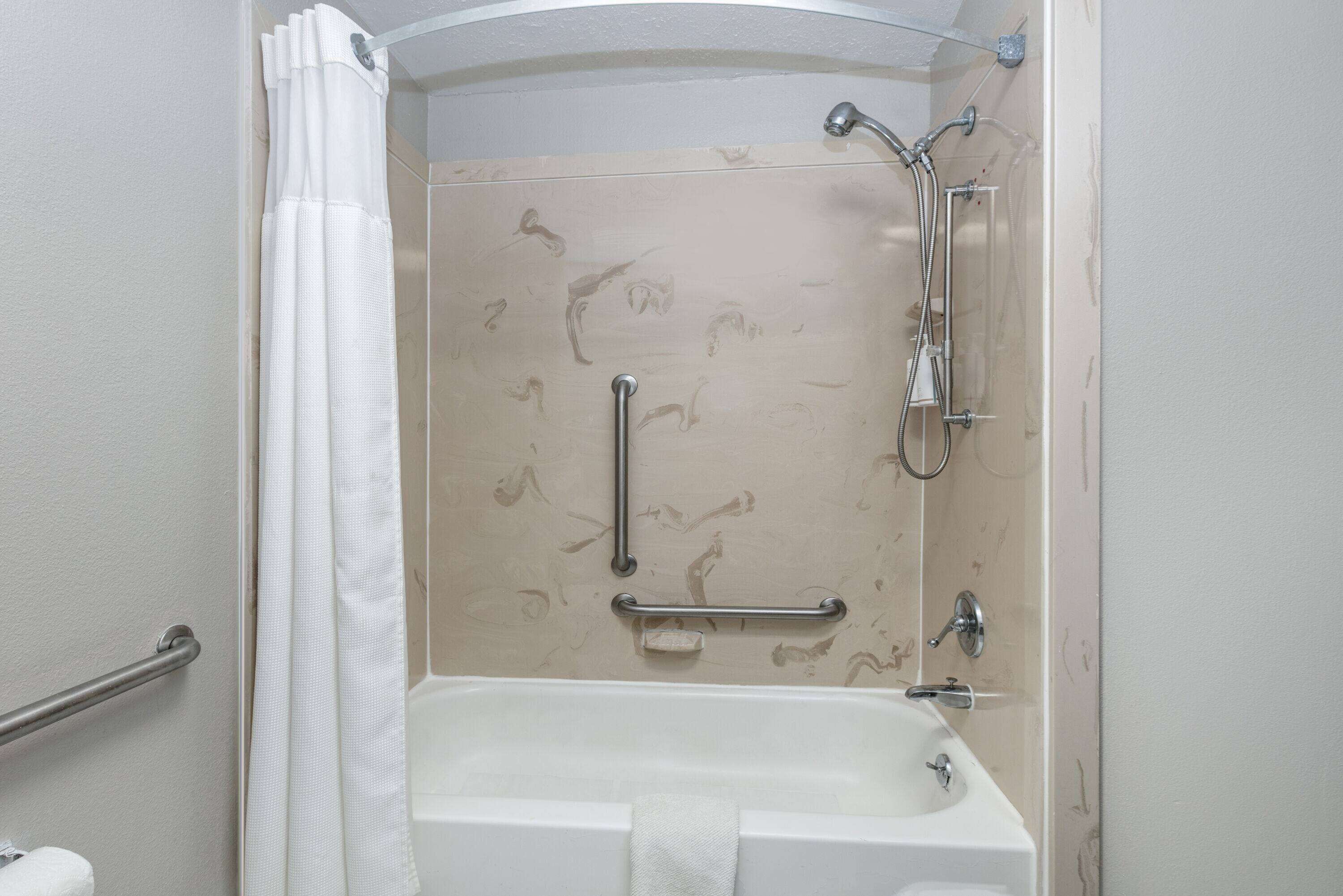 A bathroom with a bathtub, a shower, and grab bars.