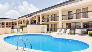 A hotel with a swimming pool, multiple balconies, and lounge chairs.