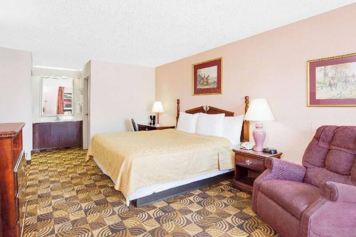 A hotel room with a bed, a chair, a desk, a lamp, and a picture on the wall.