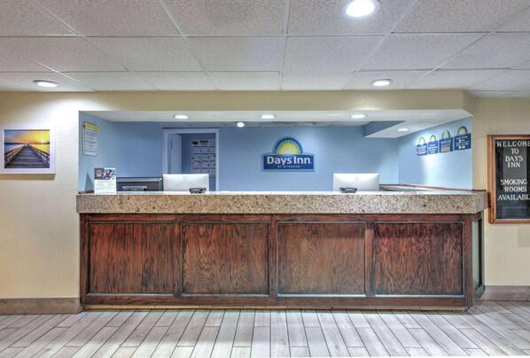 A reception area with a wooden counter, a sign for Days Inn, and a welcome sign indicating smoking rooms are available.