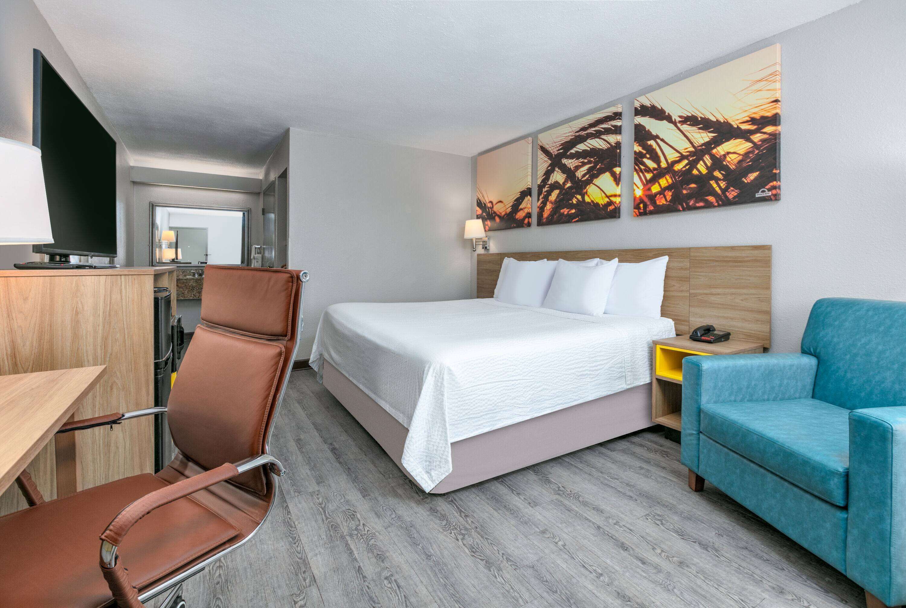 A hotel room with a bed, a desk, a chair, a TV, and artwork on the wall.