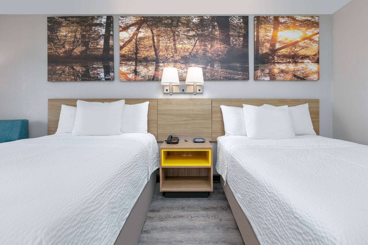 A double room with two beds, a wooden headboard, a nightstand with a lamp, and a wall-mounted phone.