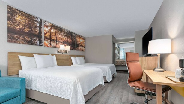 A hotel room with two beds, a desk, a chair, and artwork on the wall.