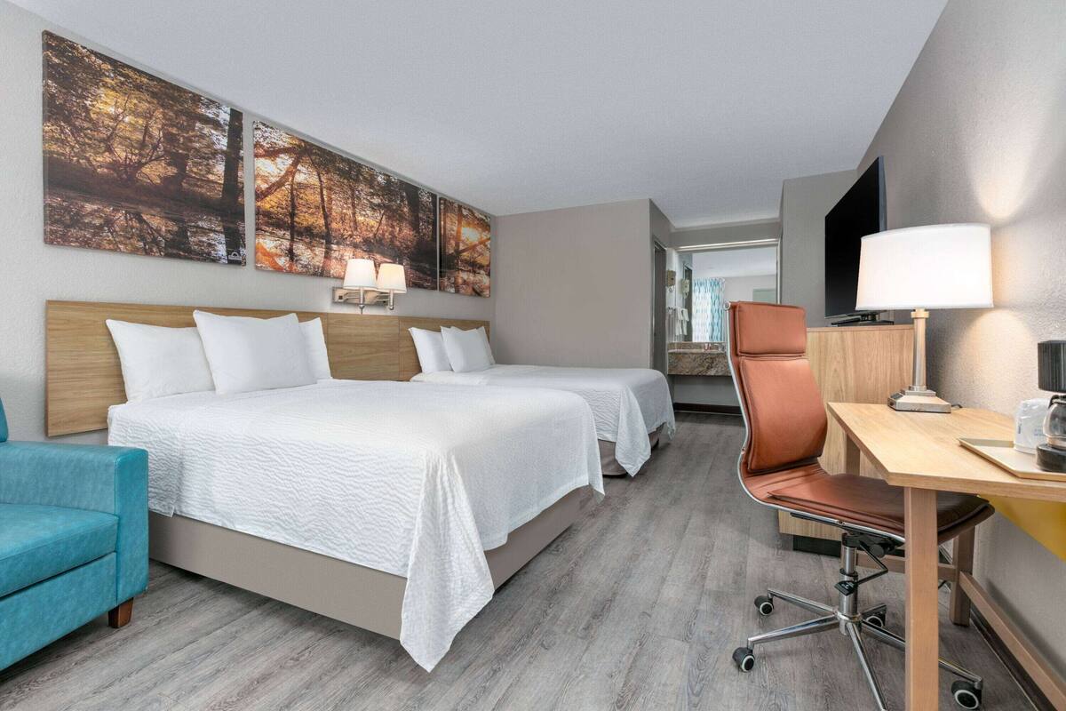 A hotel room with two beds, a desk, a chair, and artwork on the wall.