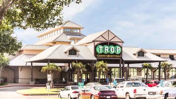 A Trop Casino Greenville building with a covered entrance, palm trees, and multiple parked cars.