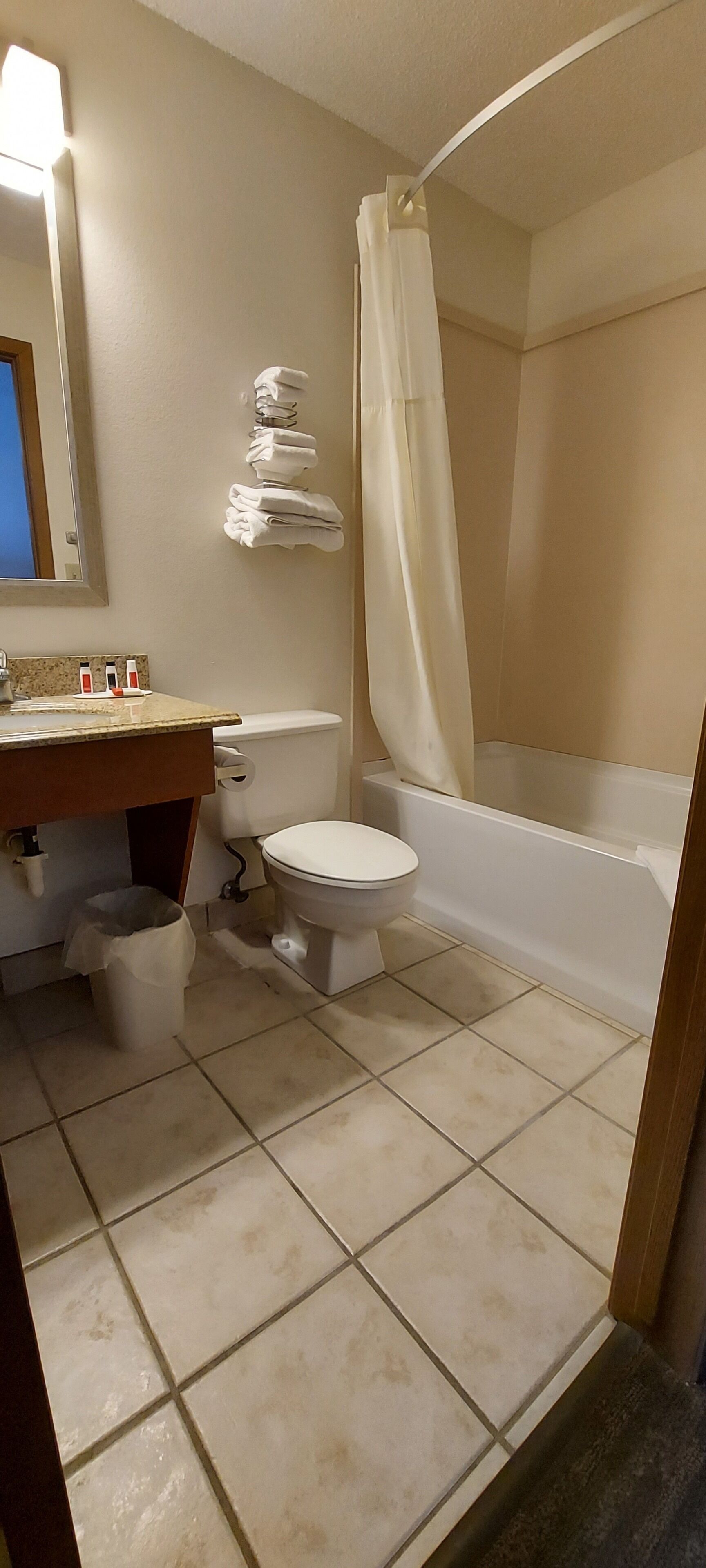 Een badkamer met toilet, wastafel en bad. Handdoekrek met opgevouwen handdoeken en douchegordijn.