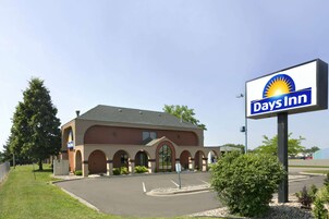 Edificio de Days Inn con un letrero llamativo, un estacionamiento y una zona ajardinada con árboles y arbustos.
