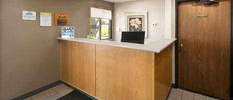 A reception desk with a wooden counter, a black computer monitor, and a framed picture on the wall.