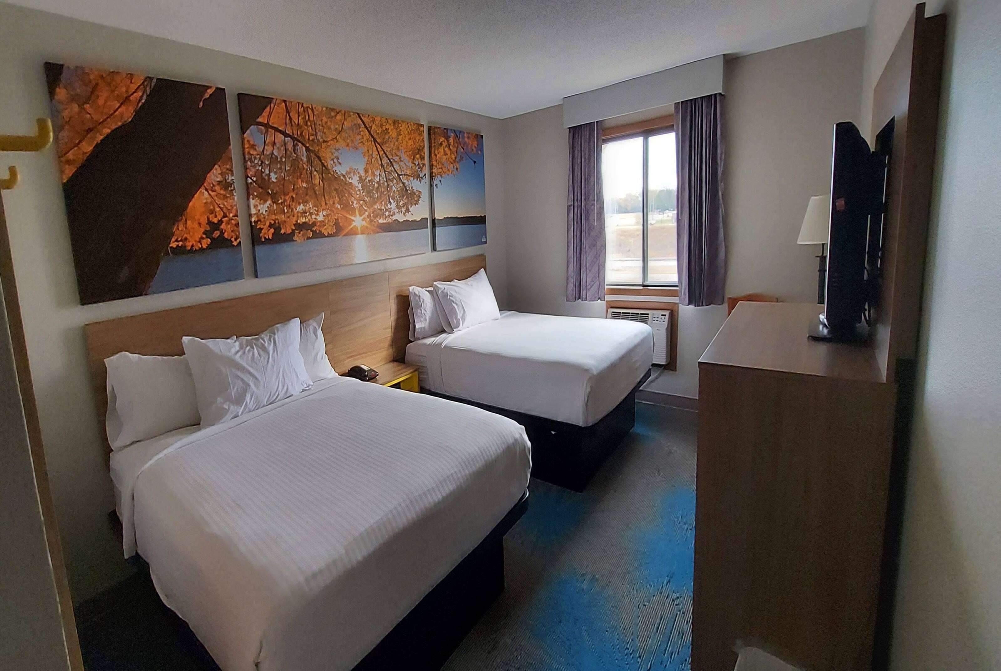 Habitación de hotel con dos camas, un ventanal con cortinas, un televisor de pantalla plana y obras de arte en la pared.