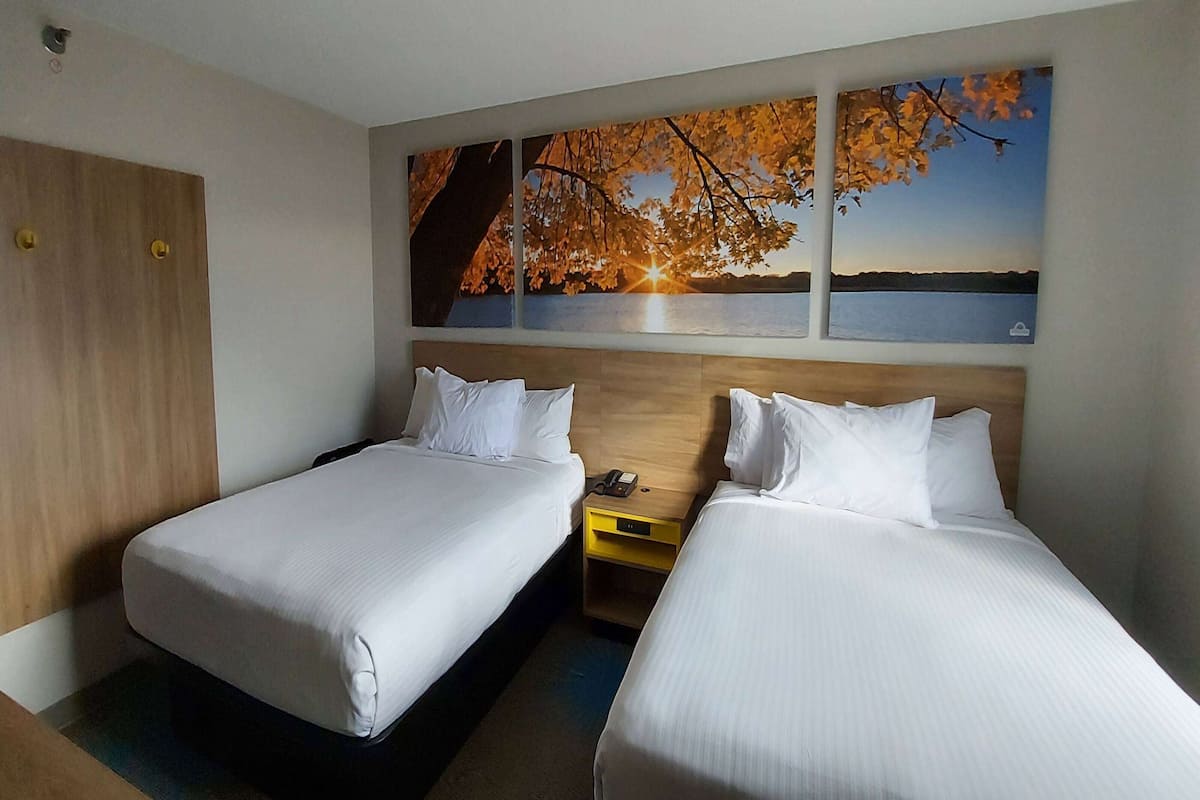 Habitación de hotel con dos camas, un armario de madera y una mesita de noche con teléfono.