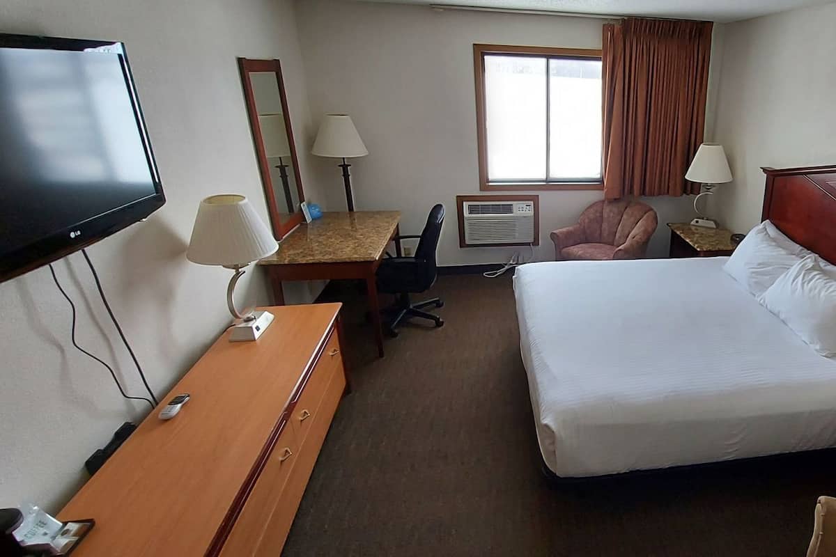 Una habitación de hotel con cama, escritorio, silla, televisor y ventana.