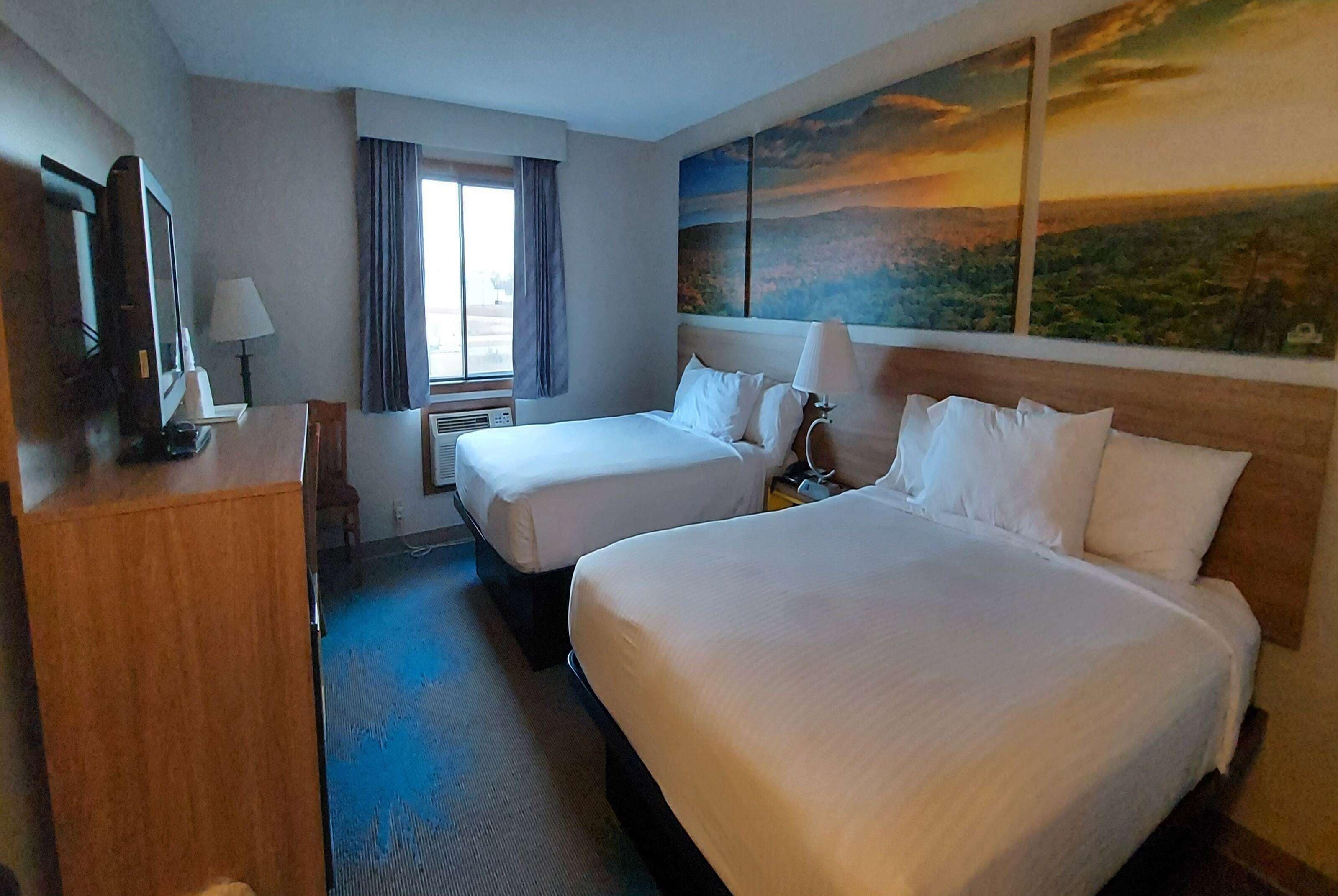 A hotel room with two beds, a desk, a TV, and a painting of a landscape.