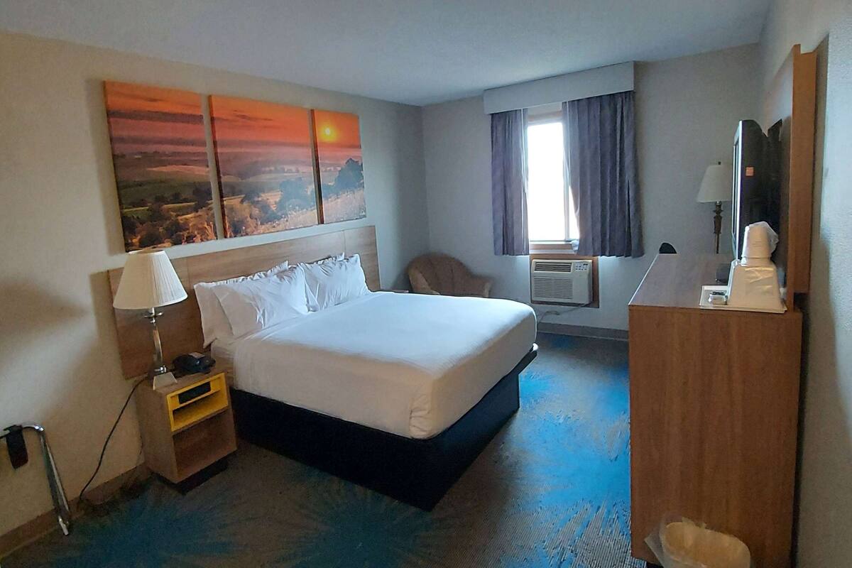 Habitación de hotel con cama, mesita de noche, lámpara, aire acondicionado y escritorio con espejo.