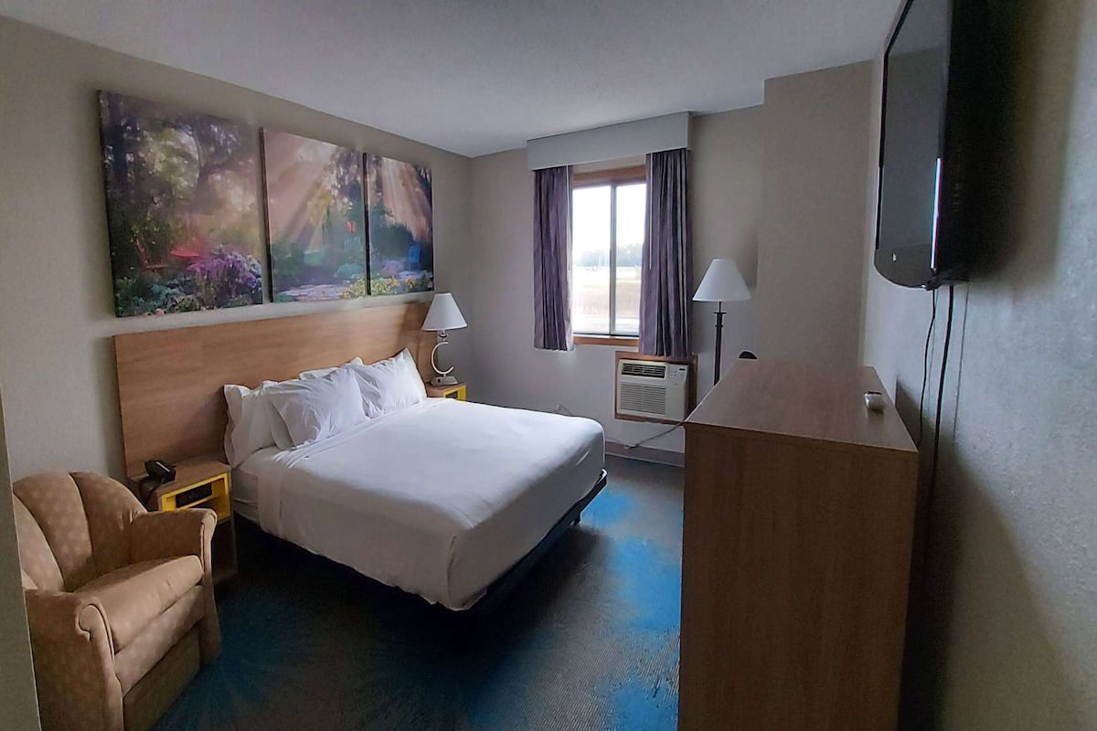 Una habitación de hotel con cama, una silla, escritorio, televisor y cuadros en la pared.