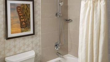 A bathroom with a toilet, bathtub, shower, and a framed picture on the wall.