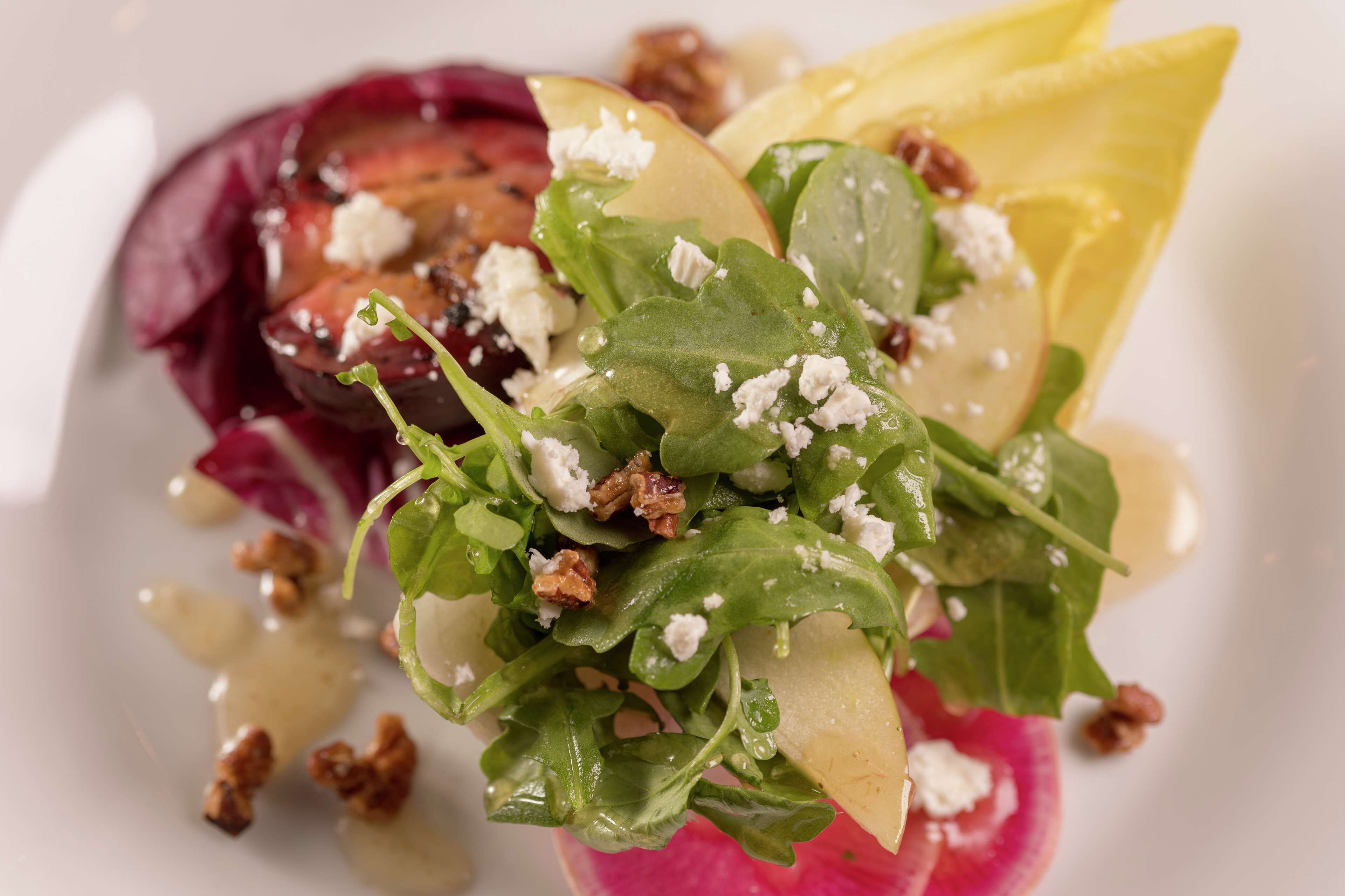 A close-up of a salad with greens, nuts, and cheese.