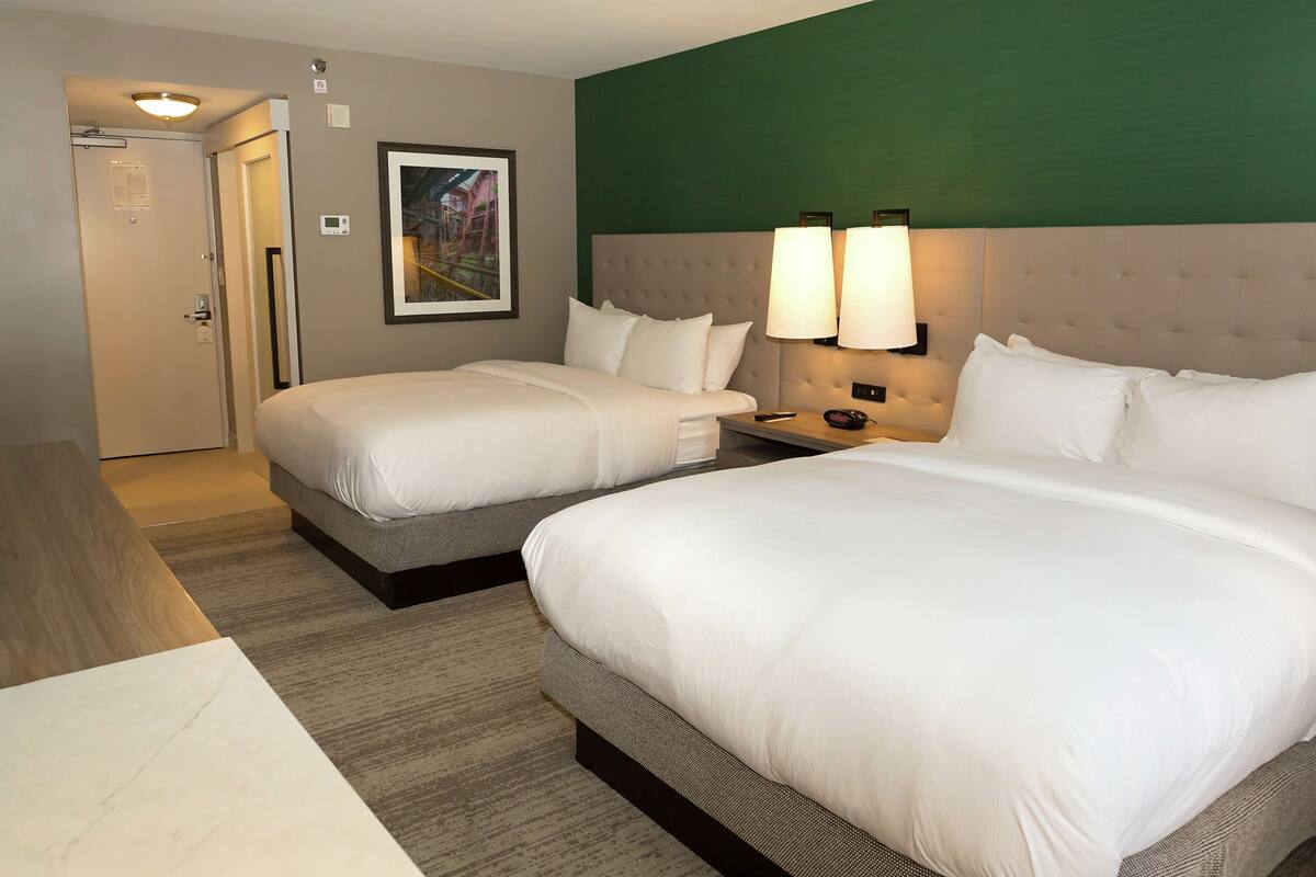 A hotel room with two beds, a wooden table, a green accent wall, and a framed picture.