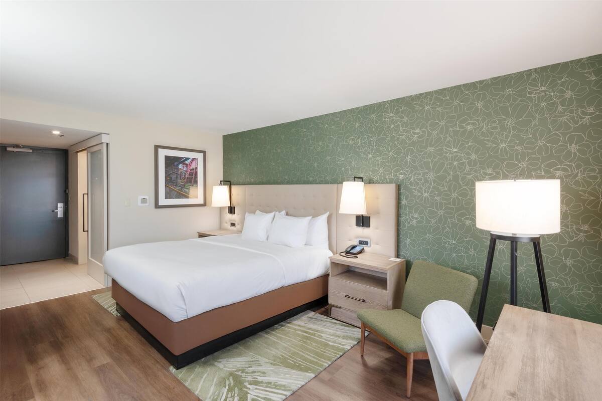 A hotel room with a bed, bedside tables, a desk, and a chair.