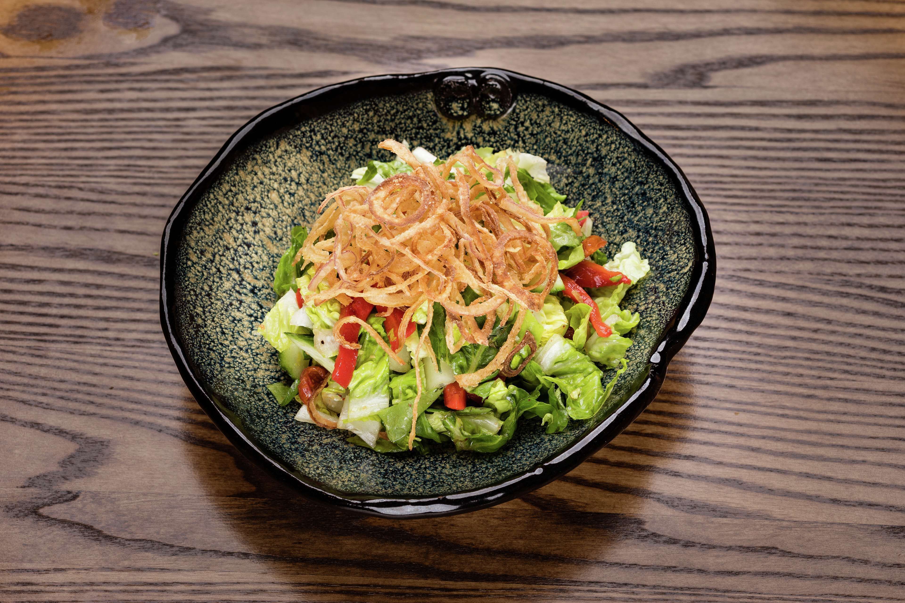 A salad in a black bowl on a wooden table.