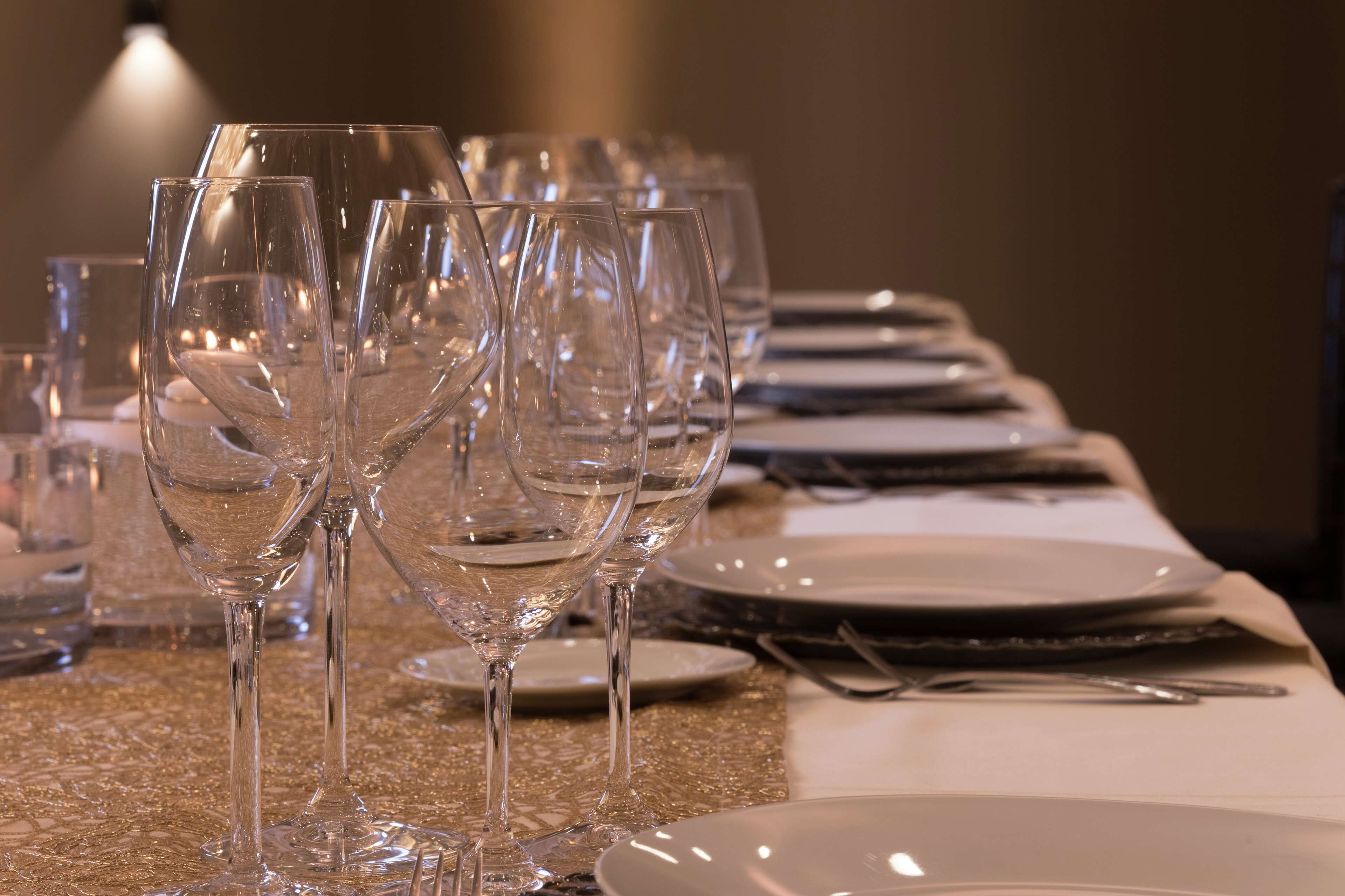 Uma mesa posta com vários copos de vinho, pratos e talheres.