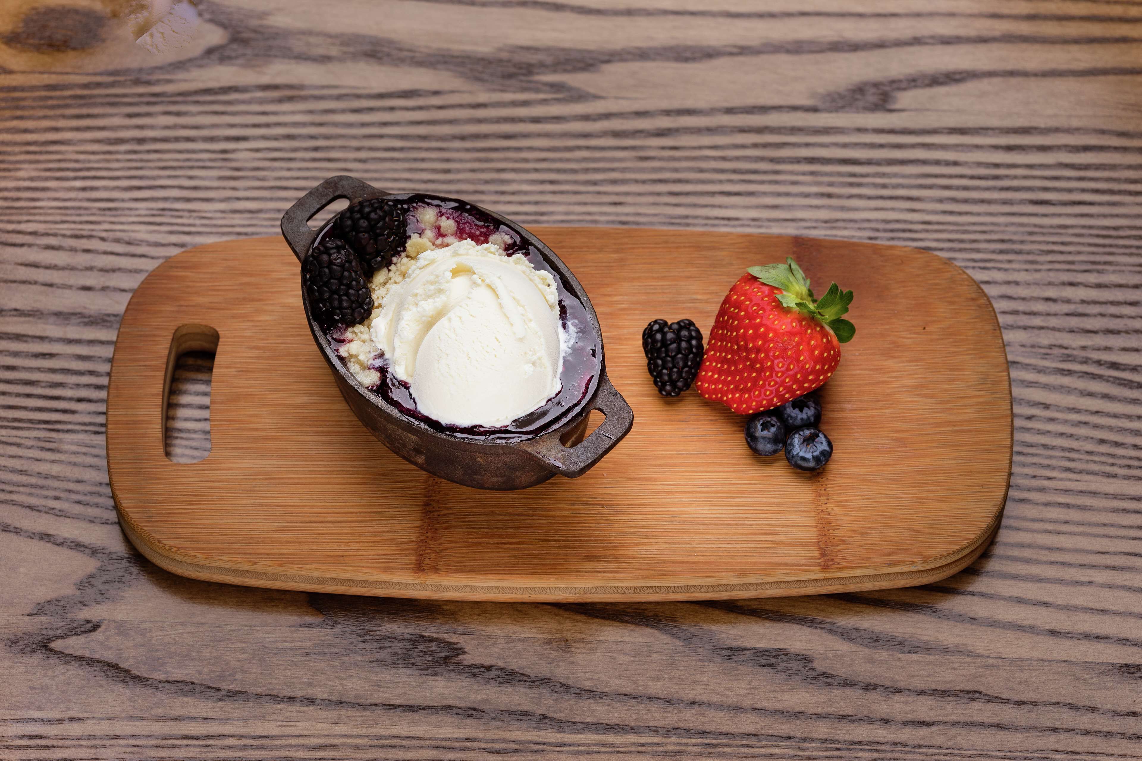 Un postre en una sartén de hierro fundido sobre una tabla de madera, acompañado de frutos rojos frescos.