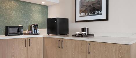 A modern kitchen with a microwave, coffee maker, and refrigerator on the counter, wooden cabinets, and a framed picture on the wall.