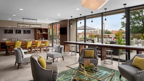 A modern hotel lobby with a bar, seating area, and large windows offering a view of the city.