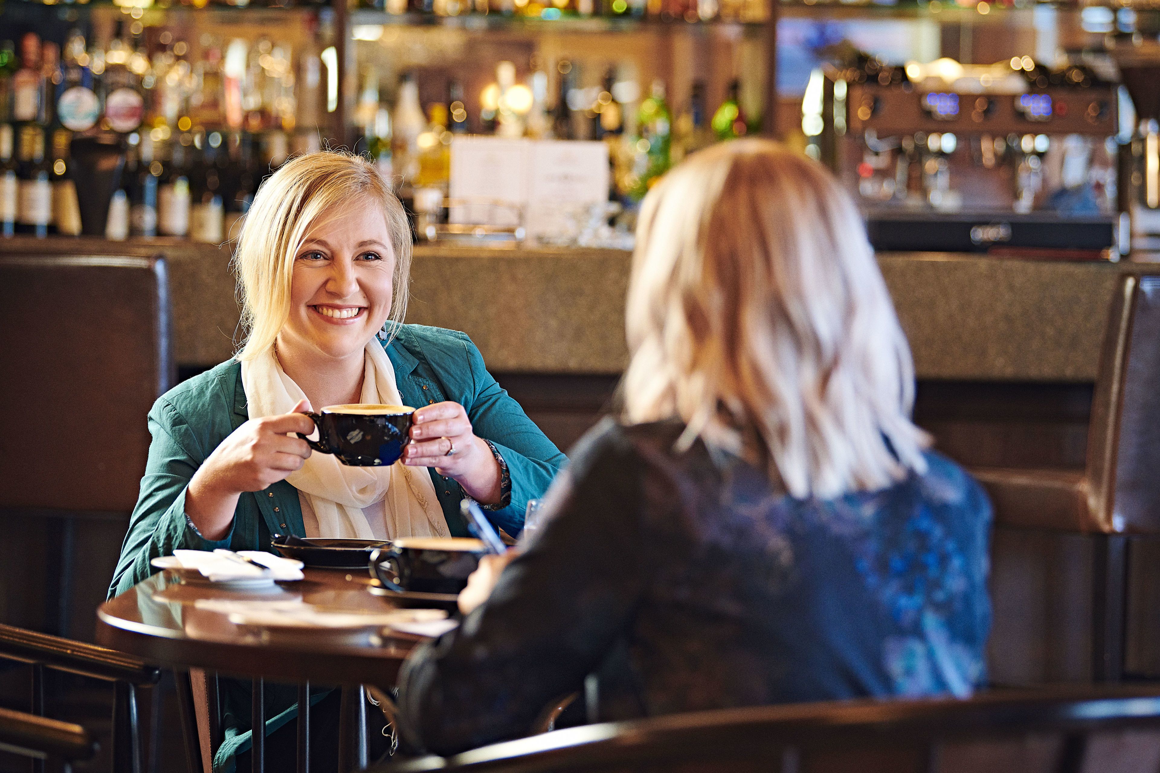 Two people sitting at a table in a bar with a bar counter and various bottles in the background.