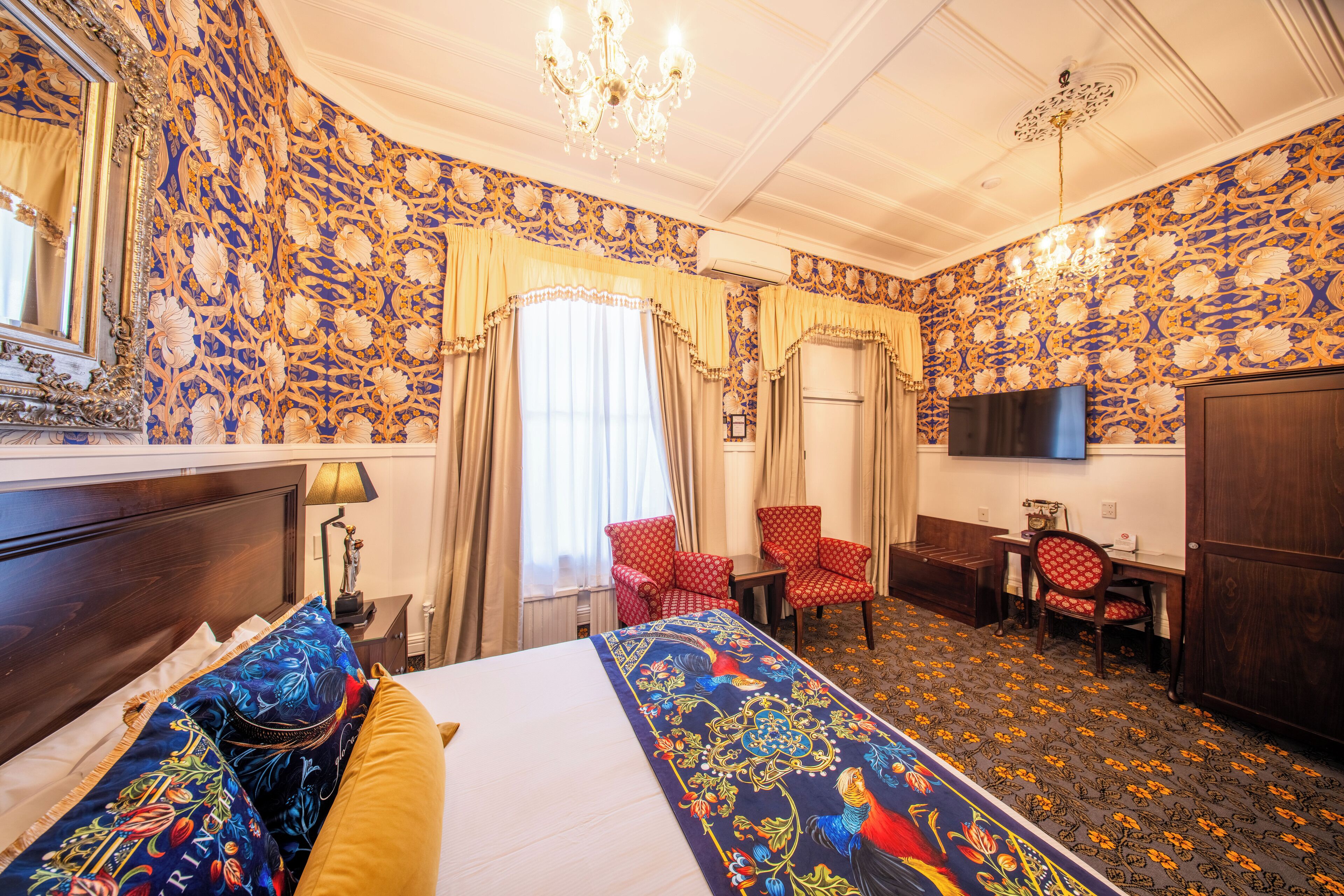 A hotel room with a large bed, two red chairs, a desk, and a TV.