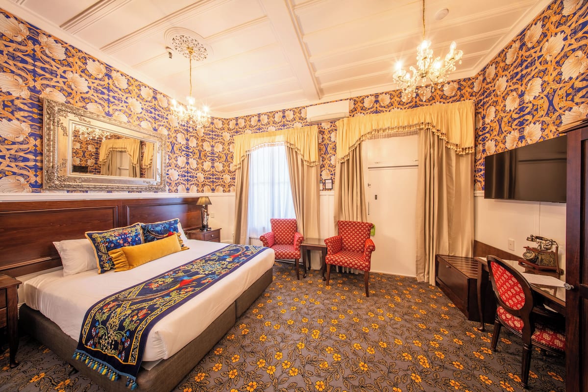 Una habitación de hotel con una cama grande, dos sillones, un escritorio, un televisor y una araña.
