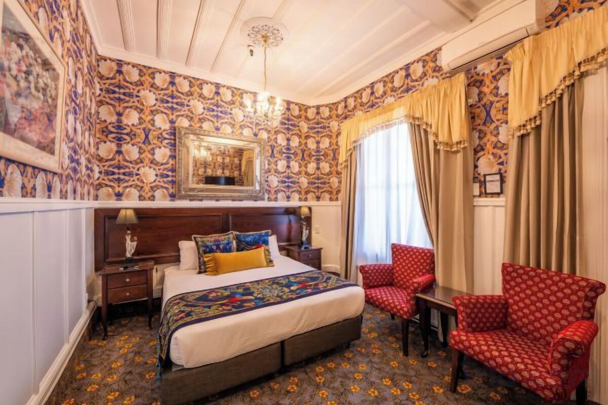 A bedroom with a large bed, a chair, a nightstand, and a mirror.