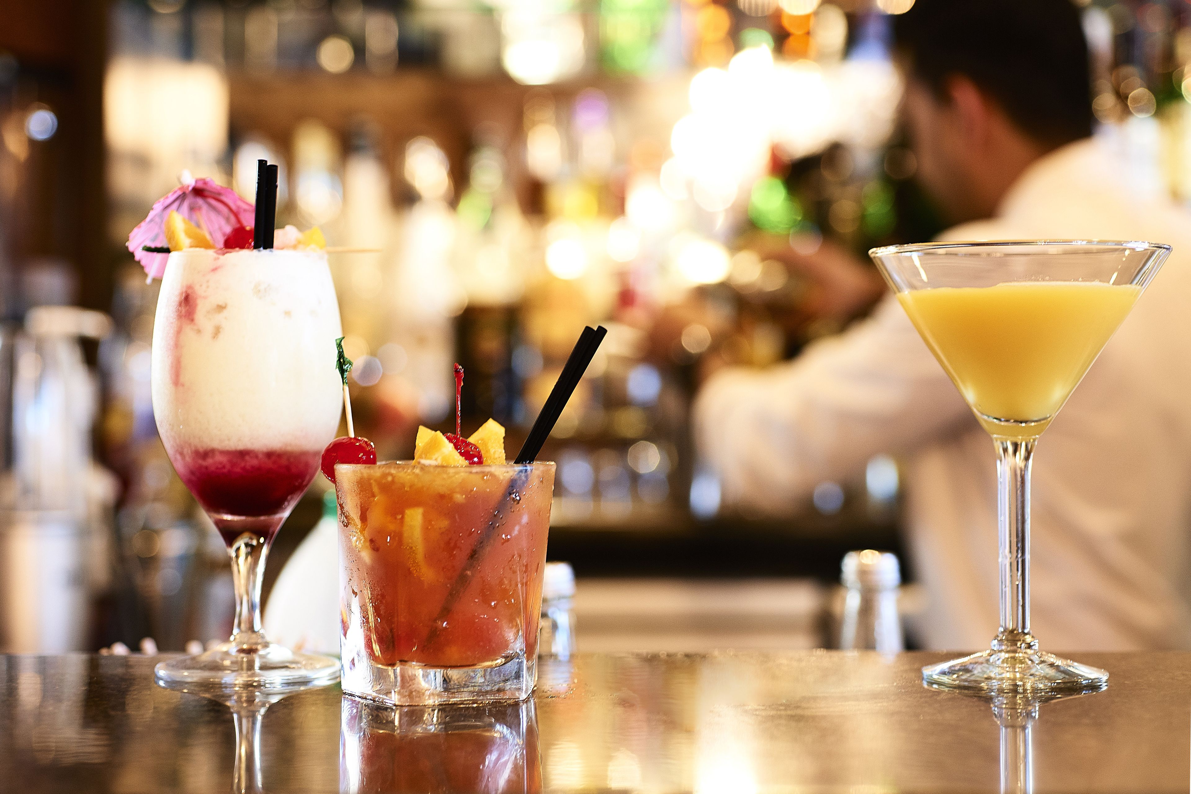 Drie cocktails op een bar, met een vage achtergrond van een bar.