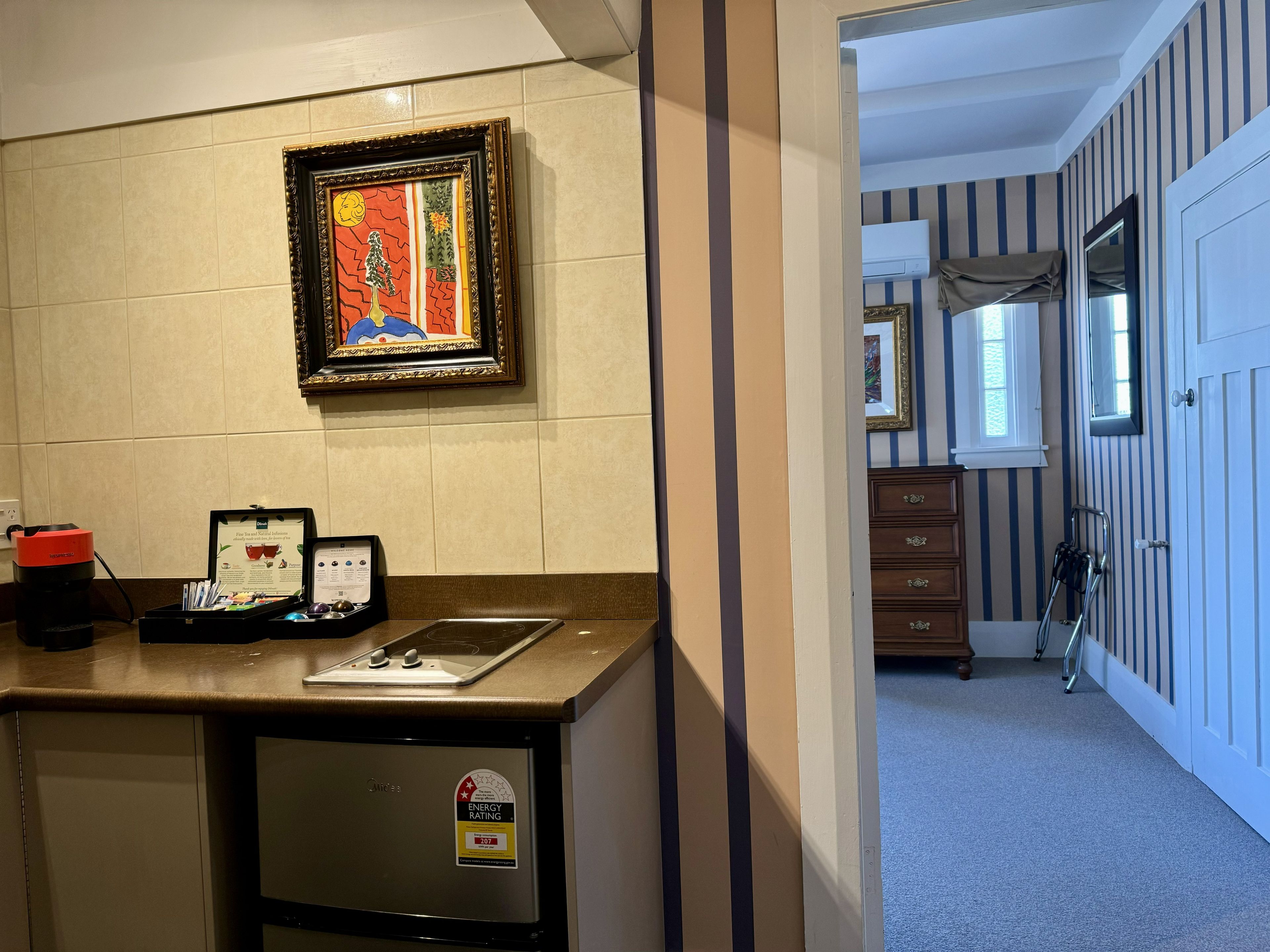 A kitchenette with a coffee maker, a framed artwork, and a refrigerator with an energy rating sticker.