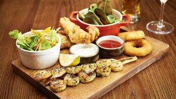 Un plateau en bois sur lequel sont disposés divers plats, notamment des crevettes grillées, des aliments frits et une salade.