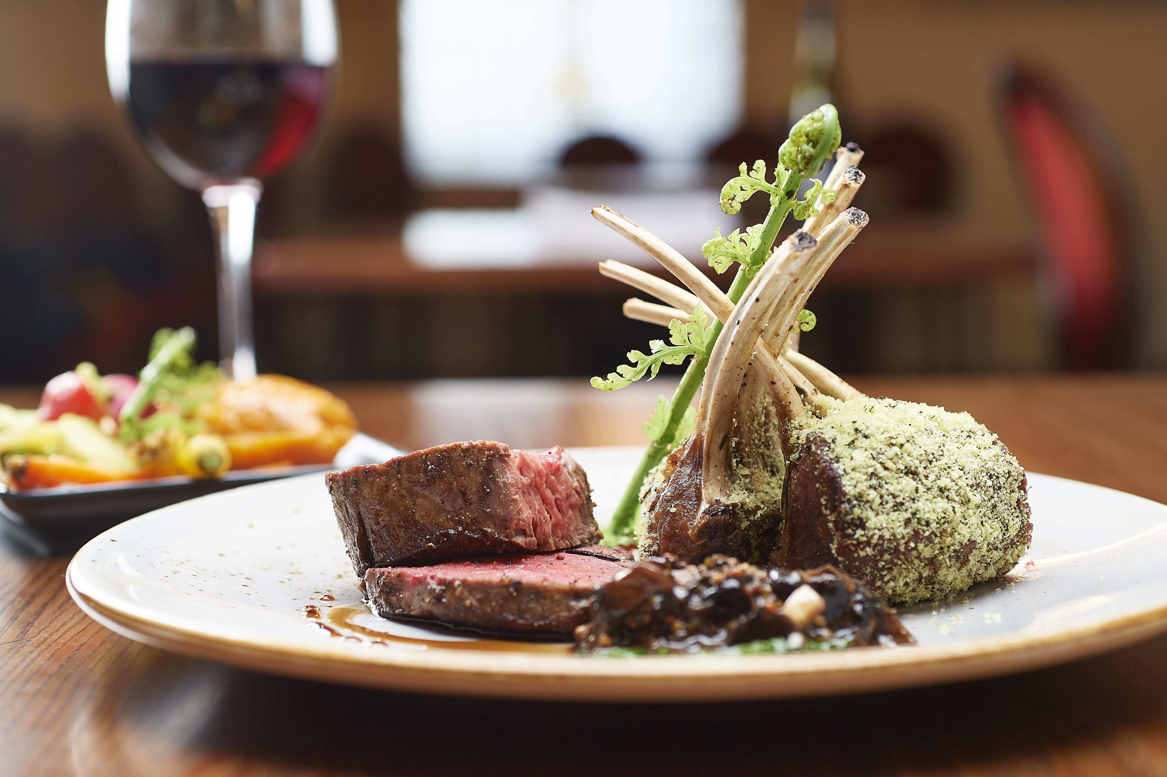 A plate of food with a piece of meat, a green vegetable, and a small dish of sauce.