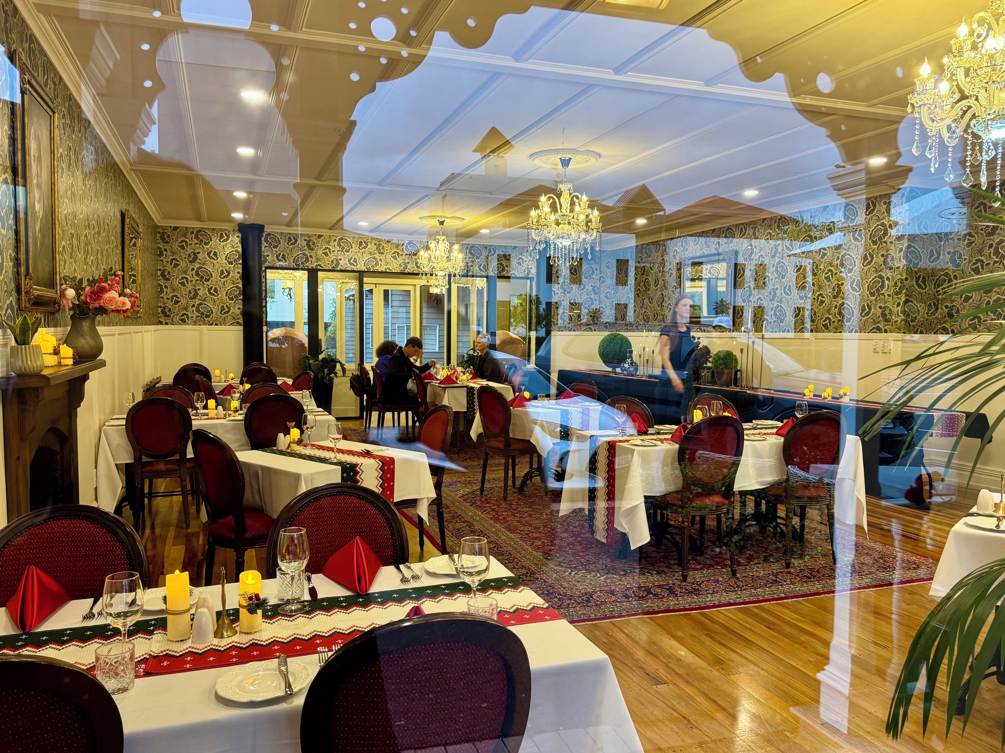 A dining area with tables set for multiple guests, chandeliers, and patterned wallpaper.