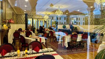 A dining area with tables set for multiple guests, chandeliers, and patterned wallpaper.
