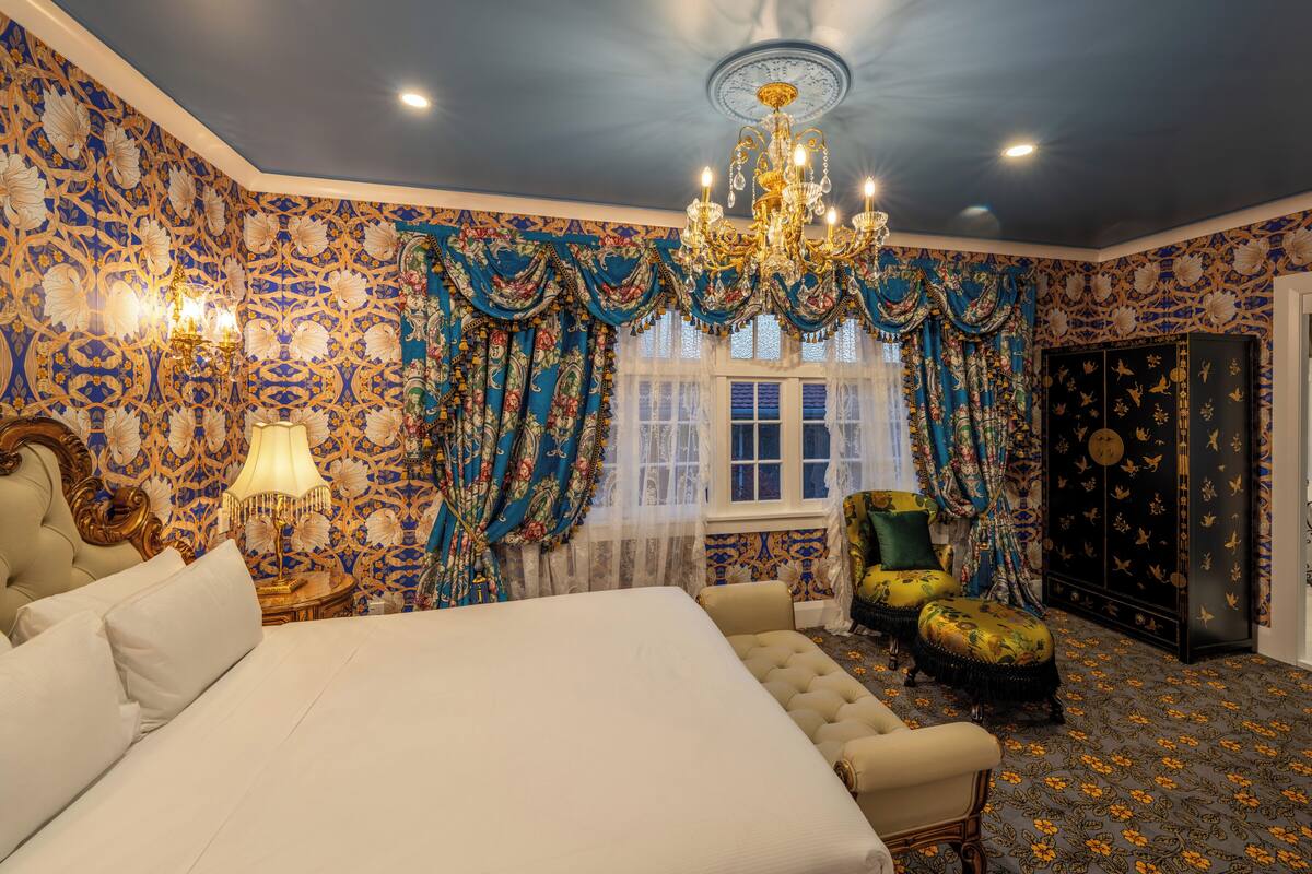 Un dormitorio lujoso con una cama grande, cortinas ornamentadas, una araña y una alfombra con estampado floral.