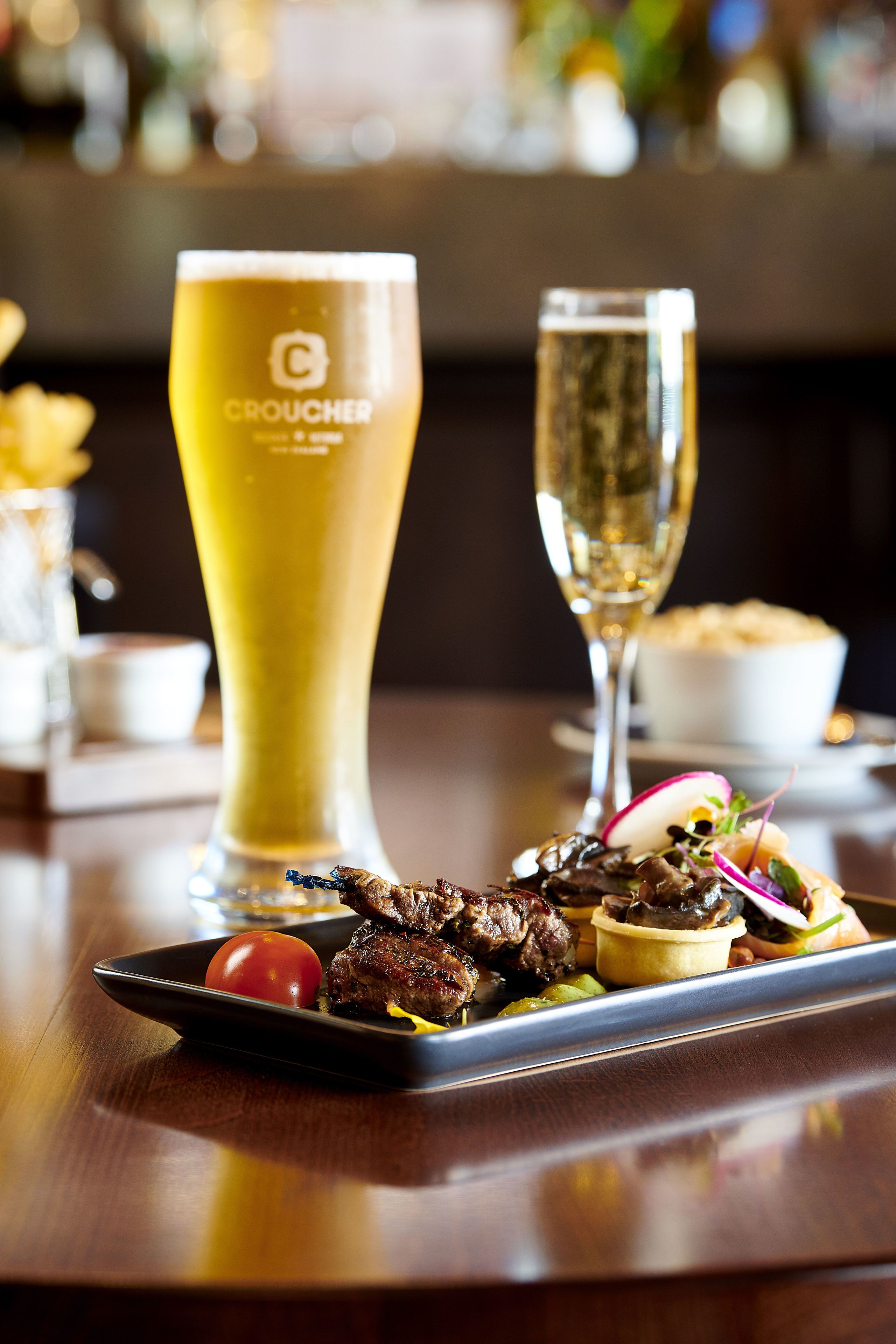 A dining table with a plate of food, a tall glass of beer, and a wine glass.