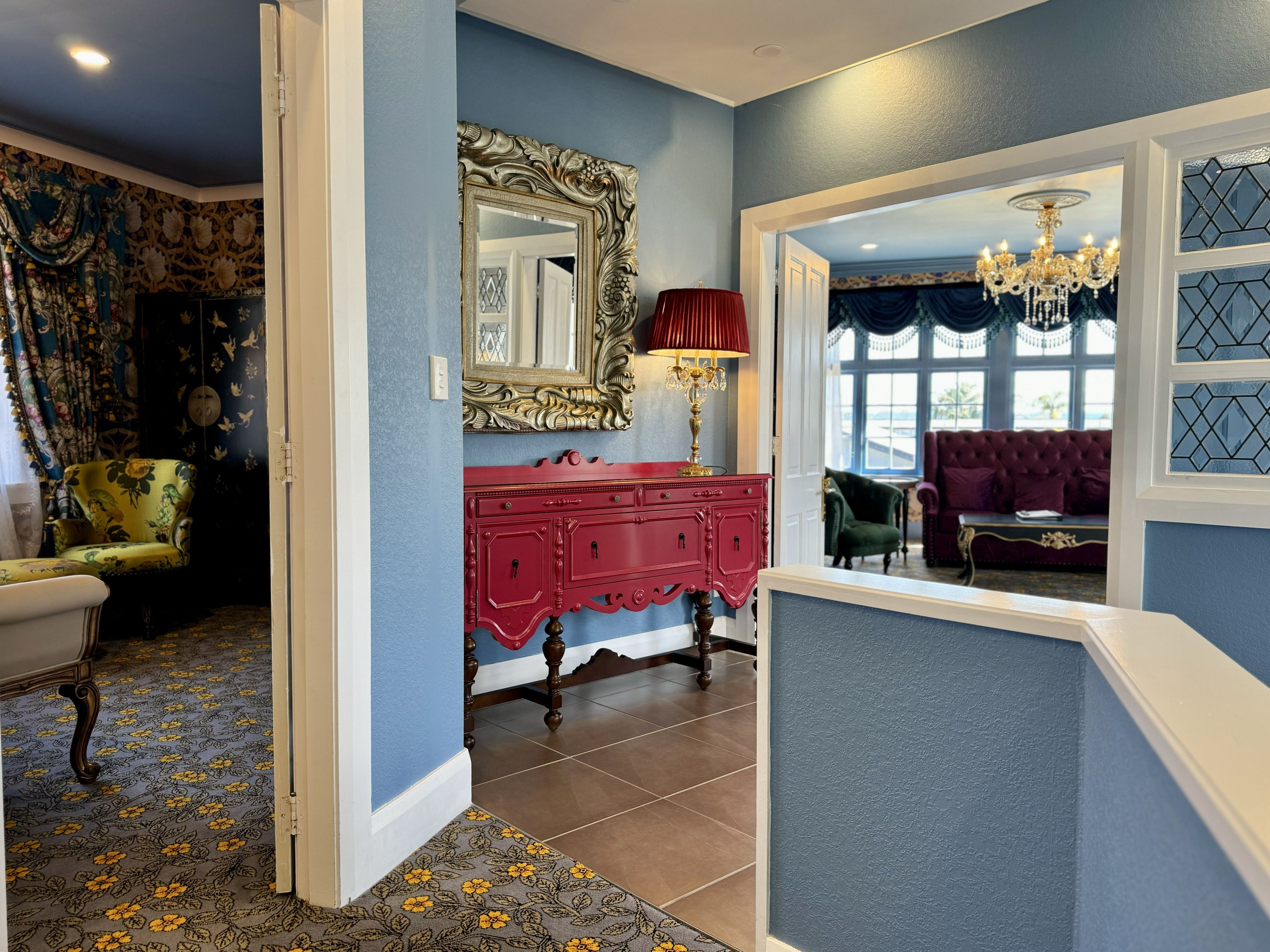 A hallway with a red dresser, a mirror, and a chandelier.