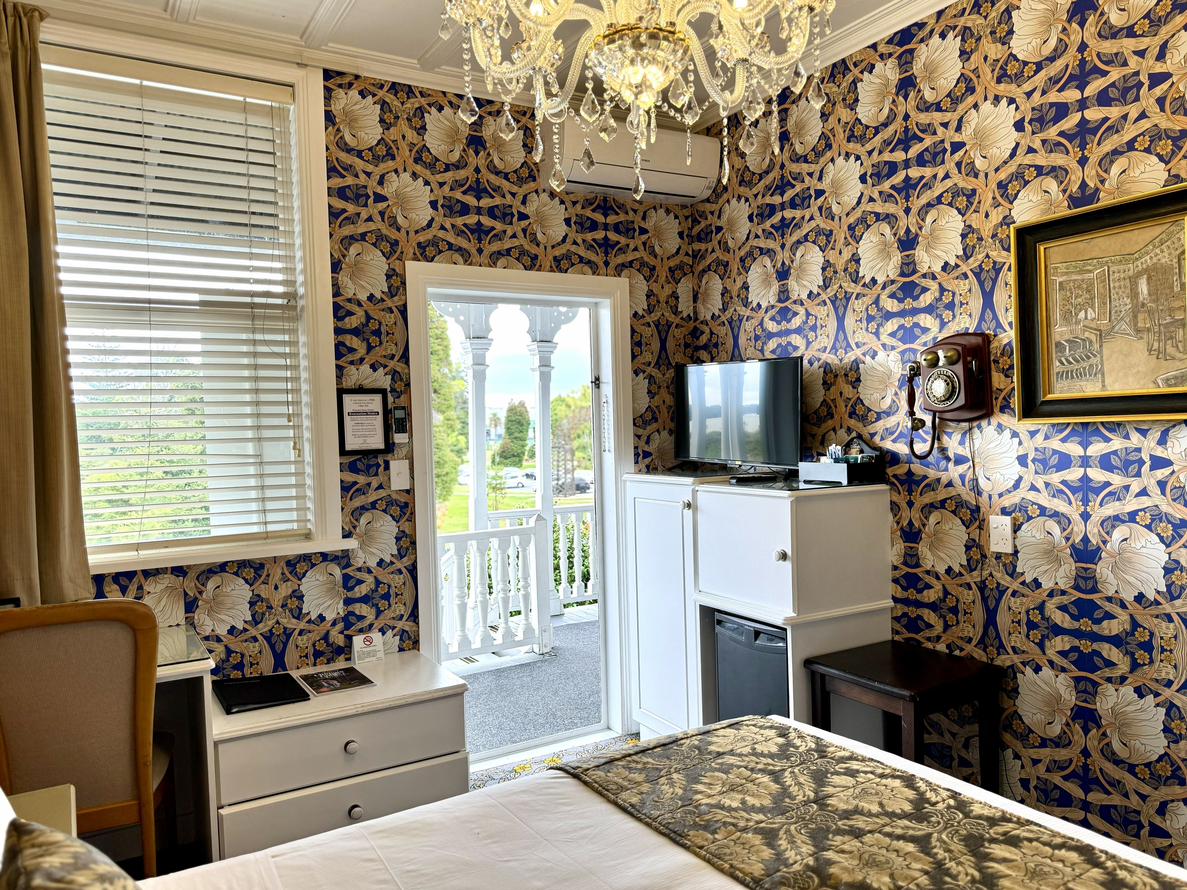 Habitación de hotel con cama, escritorio, televisor y balcón con vistas.