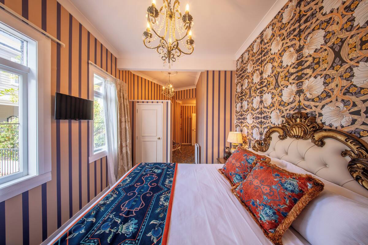 Habitación de hotel con paredes a rayas, una lámpara de araña, una cama con ropa de cama estampada y un papel tapiz floral.