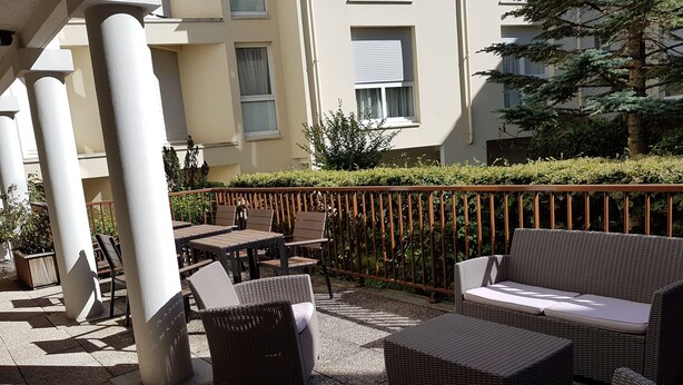 An outdoor seating area with wicker furniture and a metal railing. - ibis Château de Fontainebleau (Fontainebleau)